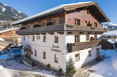 Mehrstöckiges Gebäude der Pension Schmidinger mit Holzfassade im Obergeschoss und schneebedecktem Dach.