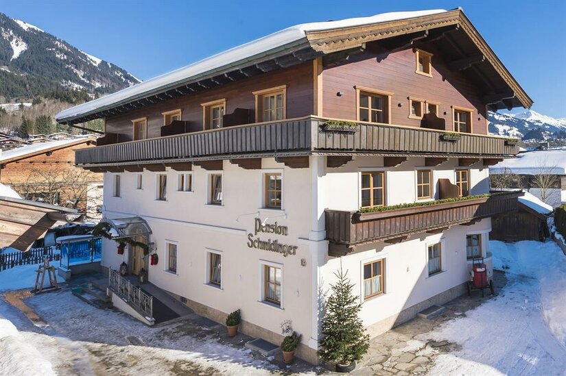 Mehrstöckiges Gebäude der Pension Schmidinger mit Holzfassade im Obergeschoss und schneebedecktem Dach.
