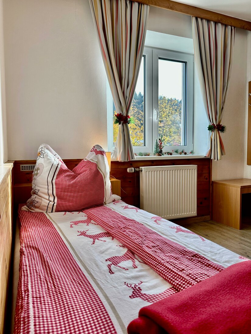 Schlafzimmer im Central Kitz Apartment Einzelbett mit rot-weißer Bettwäsche vor einem Fenster mit Vorhängen.