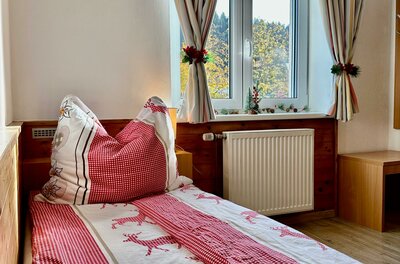 Einzelbett mit rot-weißer Bettwäsche vor einem Fenster mit Vorhängen.