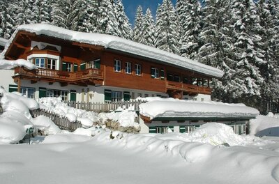 Verschneites Holzhaus mit Balkon vor einem Nadelwald im Winter.