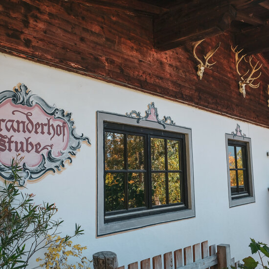 Die Fassade eines traditionellen Hauses mit dem Schild 'Branderhof Stube' und kunstvollen Fensterrahmen ist zu sehen.