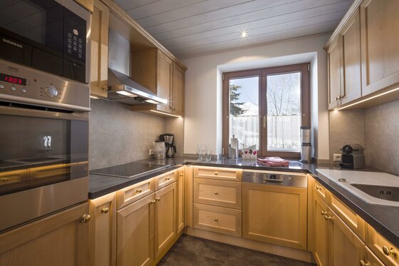 Küche im Haus Skida Moderne Einbauküche aus hellem Holz mit Backofen, Cerankochfeld und Fenster.