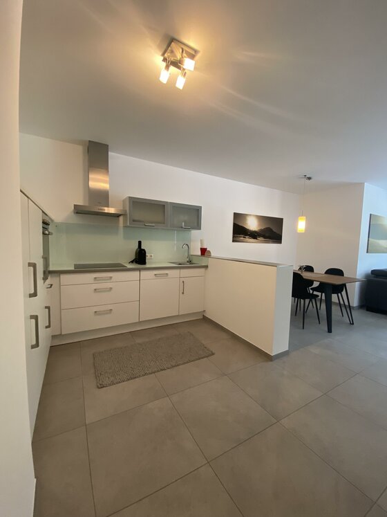 Moderne Küchenzeile im Appartement Moderne weiße Küchenzeile mit Dunstabzugshaube, Fliesenboden und angrenzendem Essbereich.