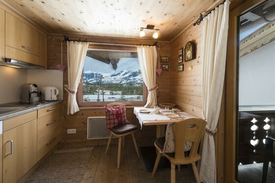 Kleine Holzküche mit Esstisch und Fenster mit Blick auf verschneite Berge.