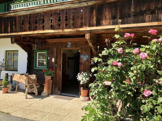 Eingangsbereich eines traditionellen Holzhauses mit Blumen und einem Balkon aus dunklem Holz.