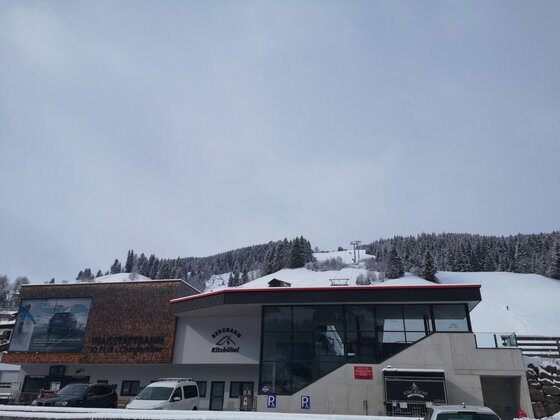 Moderne Talstation der Wagstättbahn vor verschneitem Berghang mit Nadelwald unter grauem Himmel.