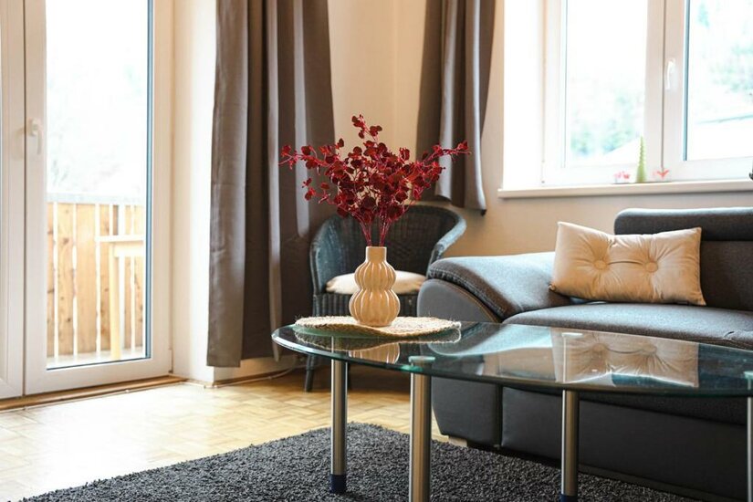 Ein heller Wohnraum mit einem grauen Sofa und einem Couchtisch. Auf dem Tisch steht eine Vase mit roten Blumen.