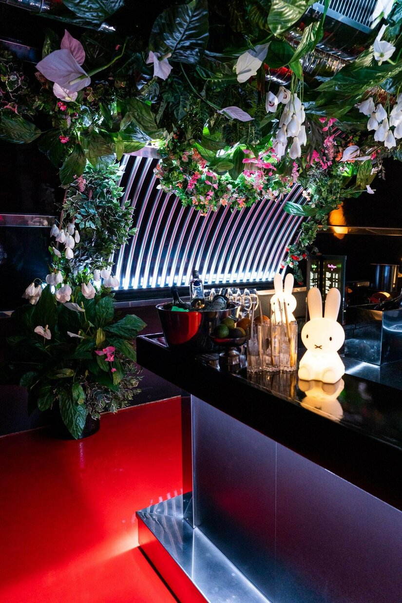 Innenansicht Club Take Five Moderne Bar mit dunklem Tresen, künstlicher Deckenbegrünung und leuchtenden Hasenfiguren.