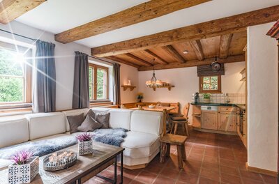 Wohnbereich im Appartement Schmidt Rustikaler Wohnraum mit weißem Ecksofa, Holzbalkendecke, Essecke und integrierter Küchenzeile.