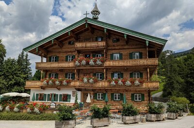 Mehrstöckiges Holzhaus im alpinen Stil mit Blumenschmuck an den Balkonen und einer Außenterrasse.