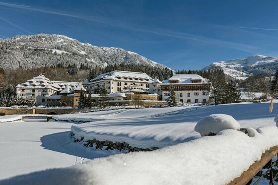 Verschneites Hotelresort vor bewaldeten Bergen unter blauem Himmel im Winter.