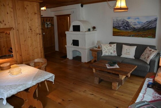 Wohnbereich im Kitzalphouse Apartment Rustikaler Wohnraum mit Holzboden, weißem Kachelofen, grauem Sofa und massivem Couchtisch.
