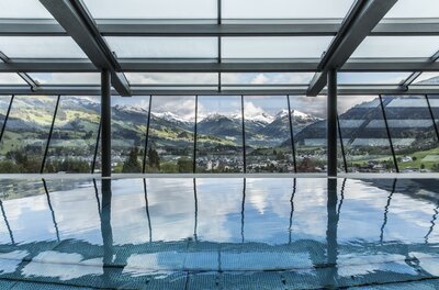Hallenbad mit Glasfront und Blick auf ein Gebirgspanorama mit schneebedeckten Gipfeln.
