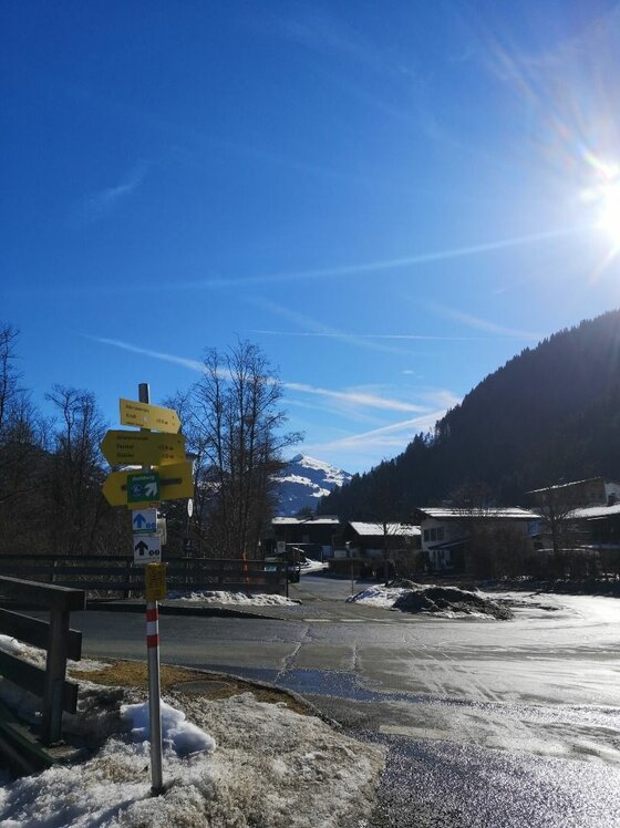 Gelbe Wegweiser an einer Straße im Winter vor Bergen und blauem Himmel.