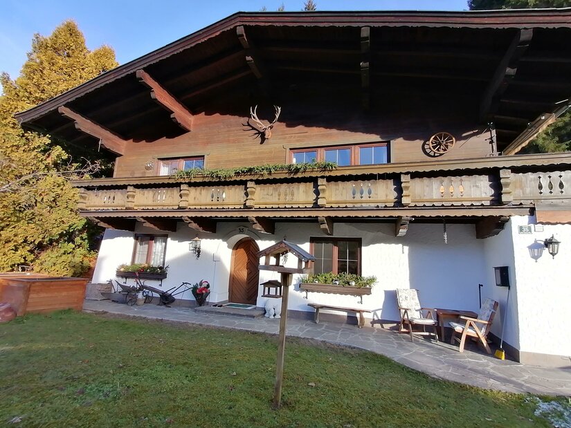 Zweistöckiges alpines Wohnhaus mit weißer Fassade im Erdgeschoss und dunklem Holzbalkon im Obergeschoss.