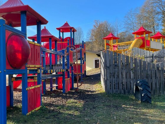 Spielplatz am Campingplatz Bunter Kinderspielplatz mit Klettergerüsten, Rutschen und Holzzaun unter blauem Himmel.