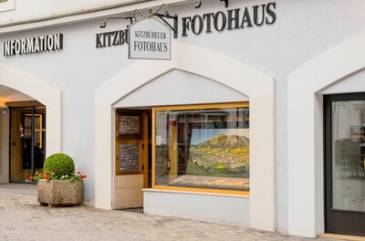 Außenansicht des Kitzbüheler Fotohauses mit Schaufenster und Firmenschild an einer hellen Fassade.