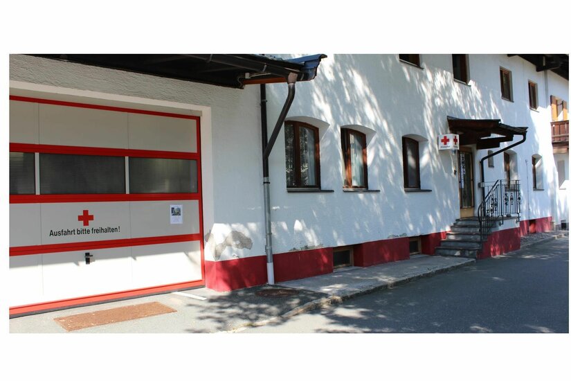 Rettungsstation Rotes Kreuz Weißes Gebäude mit Garagentor des Roten Kreuzes und Treppenaufgang.