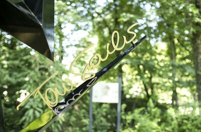 Legendenpark Ein elegantes Schild mit der Schrift "Tourists" in goldener Farbe, das vor einer grünen, bewaldeten Kulisse steht. Der ruhige Hintergrund sorgt für eine angenehme Atmosphäre.