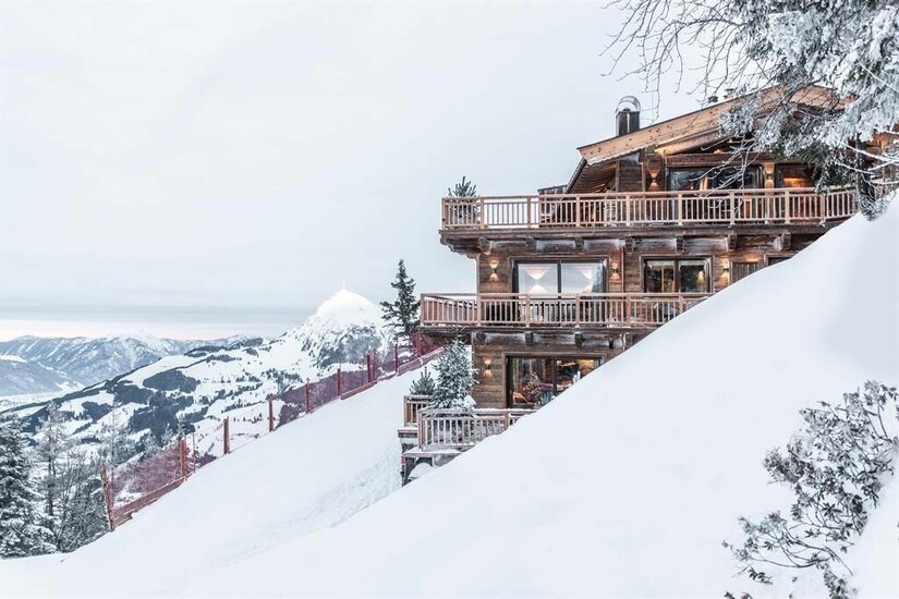 Mehrstöckiges Holzchalet an einem verschneiten Berghang mit Blick auf die Alpen.