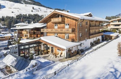 Mehrstöckiges Holzhaus mit schneebedecktem Dach und Terrasse in einer winterlichen Berglandschaft.
