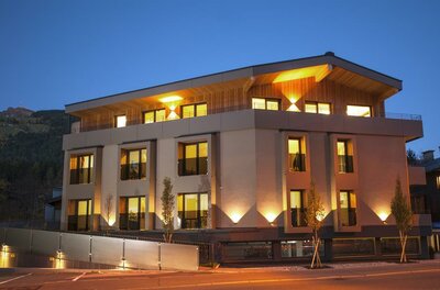 Beleuchtetes, modernes Apartmenthaus in der Dämmerung mit Holzfassade im Dachgeschoss.