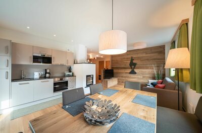 Moderner Wohn- und Essbereich mit Holztisch, Küchenzeile und Sofa vor einer Holzwand.