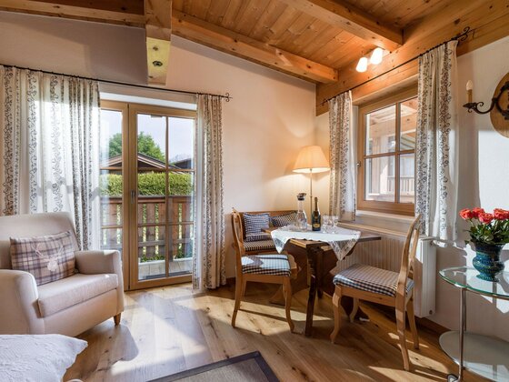Wohnbereich im Appartement Das Chalet Rustikaler Wohnbereich mit Holztisch, Stühlen, Sessel und Balkonzugang unter einer Holzdecke.