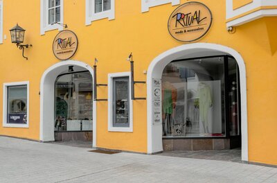 Gelbe Hausfassade mit dem Modegeschäft Ritual, Schaufenstern in Rundbögen und Firmenschildern.