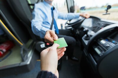 Entstrasser Ein Fahrgast gibt dem Busfahrer eine grüne Fahrkarte. Der Fahrer sitzt am Steuer des Busses.