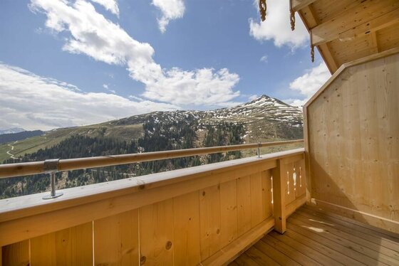 Balkonausblick Chalet Rettenstein Holzbalkon mit Blick auf bewaldete Berge und schneebedeckte Gipfel unter blauem Himmel.
