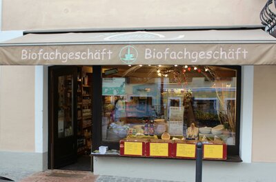 Außenansicht eines Biofachgeschäfts mit Markise, Schaufenster und Warenpräsentation im Eingangsbereich.