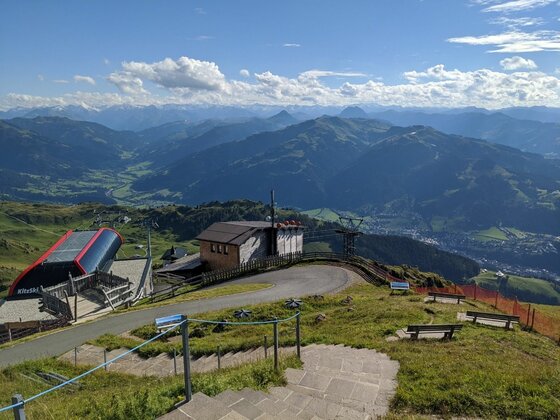 Bergstation am Hornköpfl Blick von einer Bergstation auf eine asphaltierte Straße, Gebäude und ein weites Gebirgspanorama unter blauem Himmel.