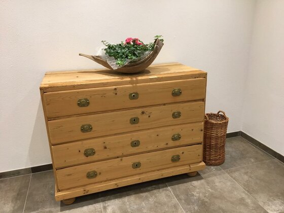 Rustikale Holzkommode mit Blumenschale und Flechtkorb in einem hellen Raum.
