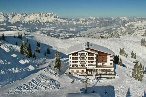 Ehrenbachhöhe im Winter Großes Hotelgebäude in einem verschneiten Skigebiet vor einem weiten Bergpanorama.