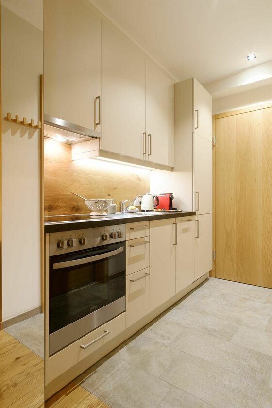 Moderne Küchenzeile in Beige mit Holzrückwand, Herd und hellen Bodenfliesen.