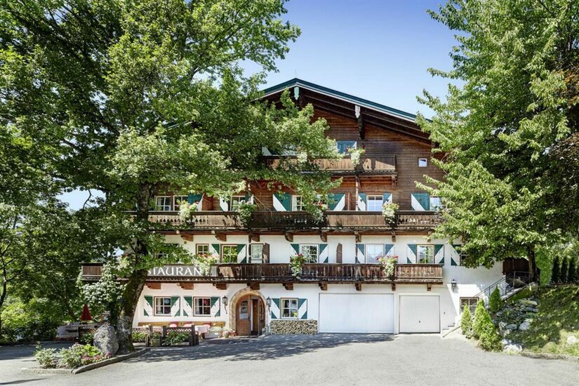 Gasthof Römerhof im Sommer Mehrstöckiges alpines Gasthaus aus Holz und Stein mit grünen Fensterläden und Blumenbalkonen hinter Bäumen.