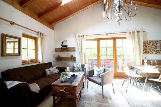 Wohnzimmer mit braunem Sofa, zwei grauen Sesseln, Holztisch und Blick auf einen Balkon.