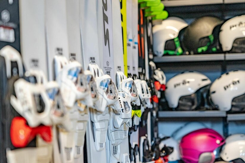 Skiverleih Sporthütte Winkler Mehrere Paar Ski in einer Halterung und Skihelme in einem Regal.