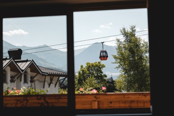 Aussicht vom Appartement Blick durch ein Fenster auf eine rote Seilbahngondel vor Gebirgskulisse.