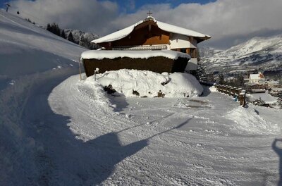 Verschneites Holzhaus mit Satteldach an einem präparierten Winterweg in den Bergen.