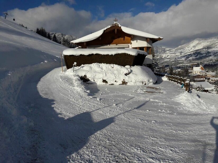 Verschneites Holzhaus mit Satteldach an einem präparierten Winterweg in den Bergen.