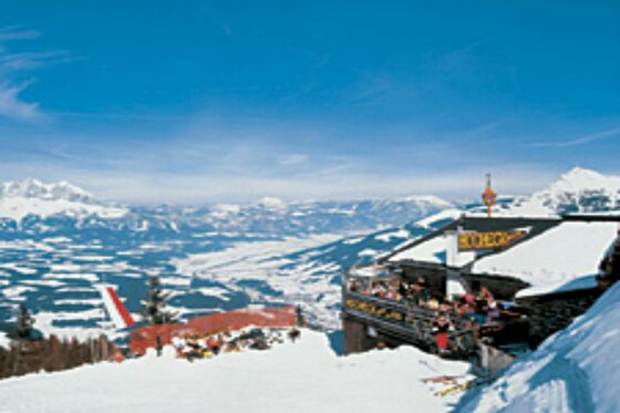 Hocheckhütte im Winter Blick von einer verschneiten Berghütte auf ein weites Tal und schneebedeckte Berggipfel unter blauem Himmel.
