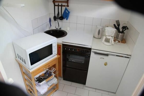 Kleine Küchenzeile mit Mikrowelle, Herd, Spüle und Kaffeemaschine.