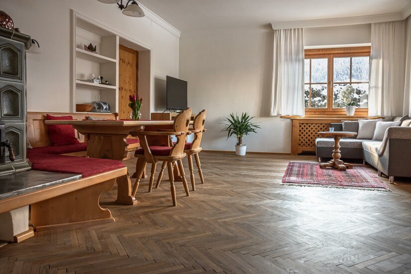 Haus Gantschnigg Wohnzimmer Wohnzimmer mit Holzesstisch, Eckbank, Kachelofen und Sofa auf Parkettboden.