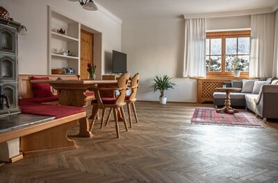Wohnzimmer mit Holzesstisch, Eckbank, Kachelofen und Sofa auf Parkettboden.