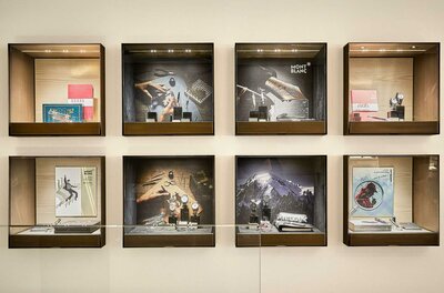 Montblanc Boutique Vitrinen Acht quadratische Glasvitrinen an einer hellen Wand mit Schreibgeräten, Uhren und Markenmotiven von Montblanc.
