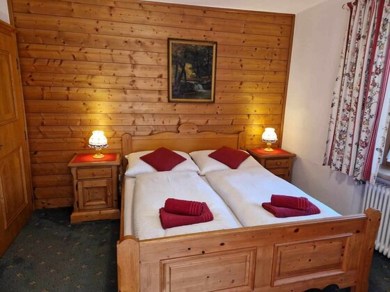 Schlafzimmer in Pension Alpenrose Doppelbett aus Holz vor einer holzgetäfelten Wand mit zwei Nachttischen und Lampen.