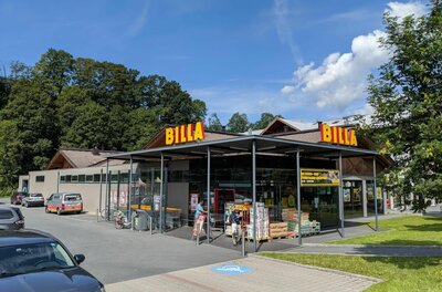 Billa Jochbergerstraße Außenansicht eines Billa-Supermarktes mit Parkplatz und bewaldetem Hintergrund unter blauem Himmel.